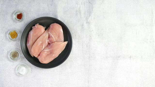 A plate of chicken breasts, with a variety of seasonings in small bowls to the left-hand side.