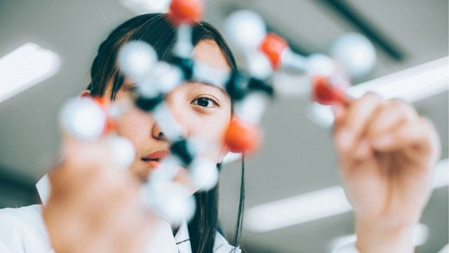 A researcher holds up a chemical structure of a molecule.