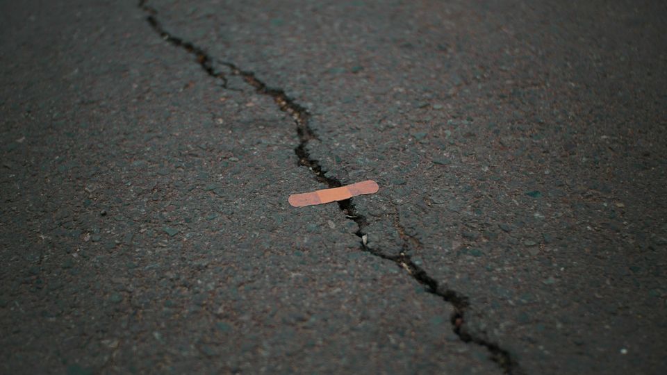 Orange band aid on concrete surface crack.