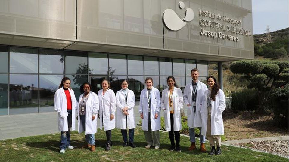 A group of scientists in lab coats stand on the grass outside a building.