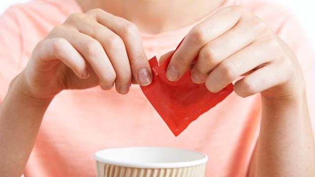 A woman tears open a packet of artificial sweetener above a coffee cup. 