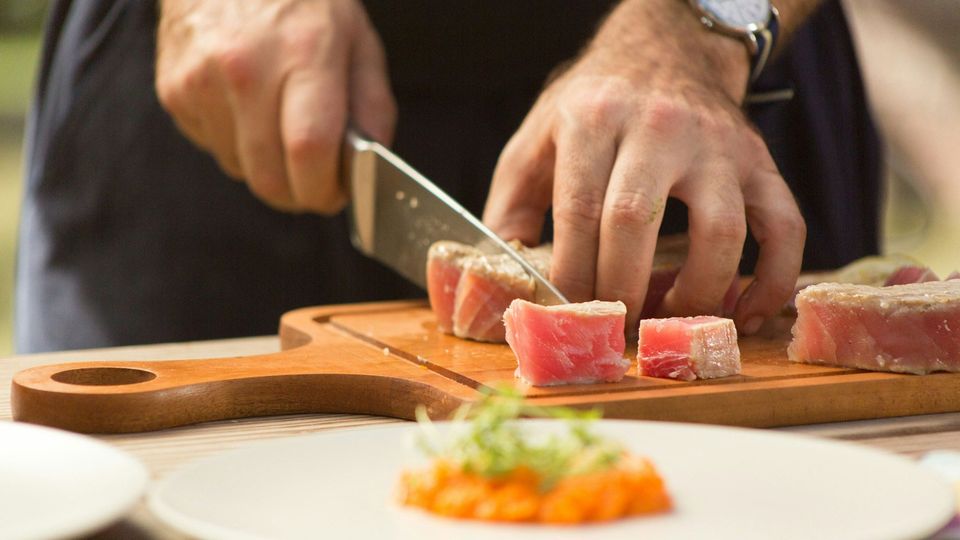 A person slices raw fish on a wooden cutting board.