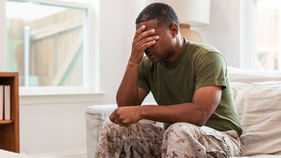 A soldier sitting on a couch holding his hand over his eyes.