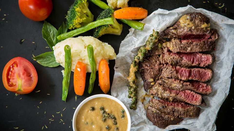 A steak dinner, with vegetables and sauce.