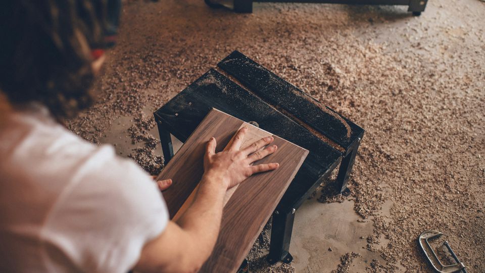 A carpenter working in a workshop with sawdust on the floor.