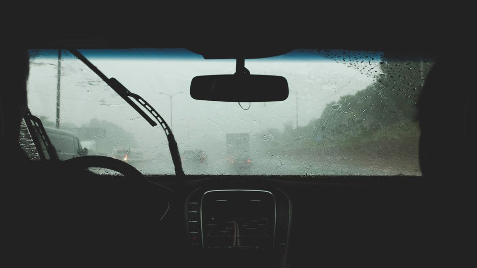 A photo taken from the backseat of a car, as the car drives through heavy rain. 