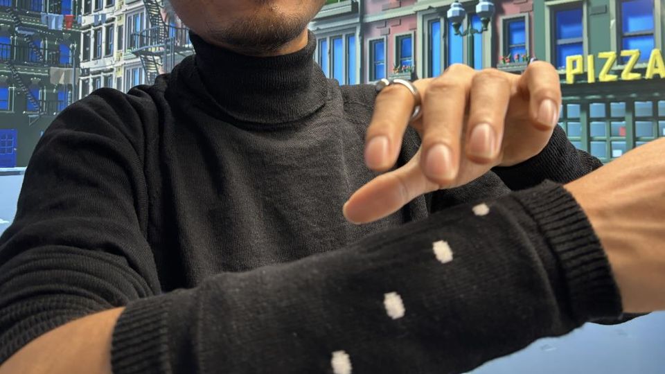 A researcher poses with the knitted sleeve over his arm, waving his other hand's fingers above it.