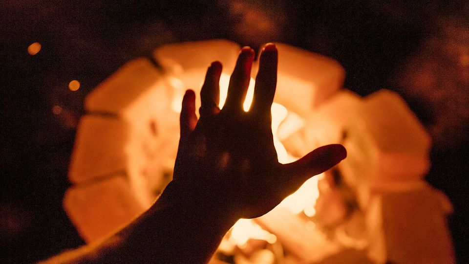 A hand reaches towards a fire.