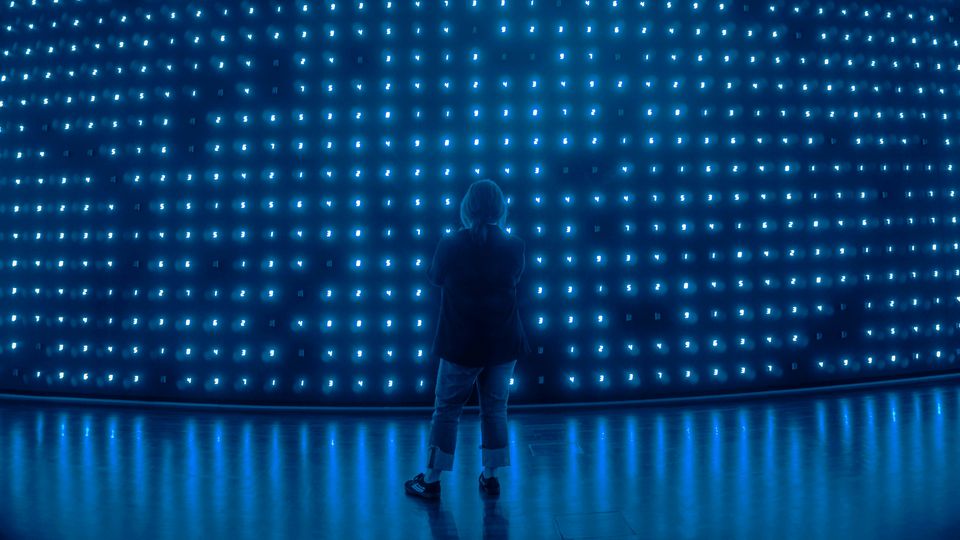 A woman stands in front of a wall covered in blue LED numbers