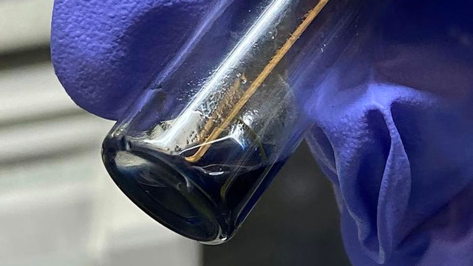 A sample vial with a small amount of purple/blue solution, containing crystals of berkelocene.