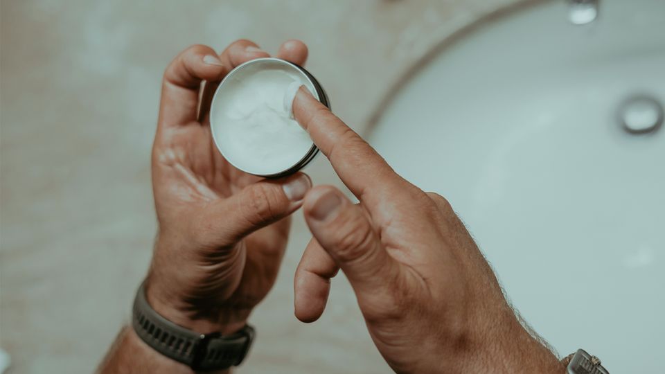A man dipping a finger into a pot of skincare cream containing a natural ingredient that could help treat skin lupus.