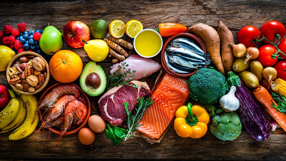 Selection of healthy foods on a wooden table, including fruits, vegetables, nuts and fish.