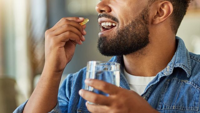 Man taking a vitamin D capsule with a glass of water in a bright indoor setting. 