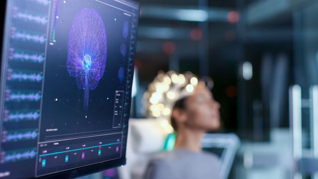 Woman undergoing brain stimulation therapy with neural activity visualized on a nearby digital screen.