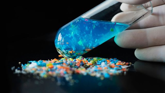 Colorful shreds of plastic on a black surface. Blue test tube vial and gloved hand visible. 