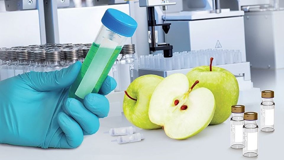 Gloved hand holding vial near green apples and lab instruments, illustrating micro-SPE technology for optimizing food safety testing.