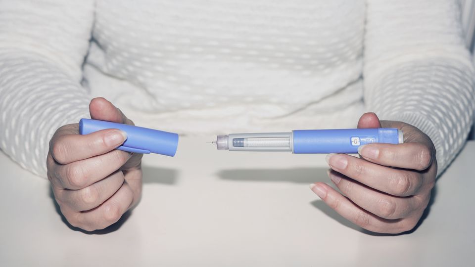 Person holding a GLP-1 injectable pen, ready for use, with cap removed.