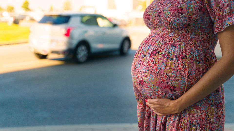 Pregnant woman standing outdoors with hand on her belly, near a car, highlighting concerns of air pollution on pregnancy.