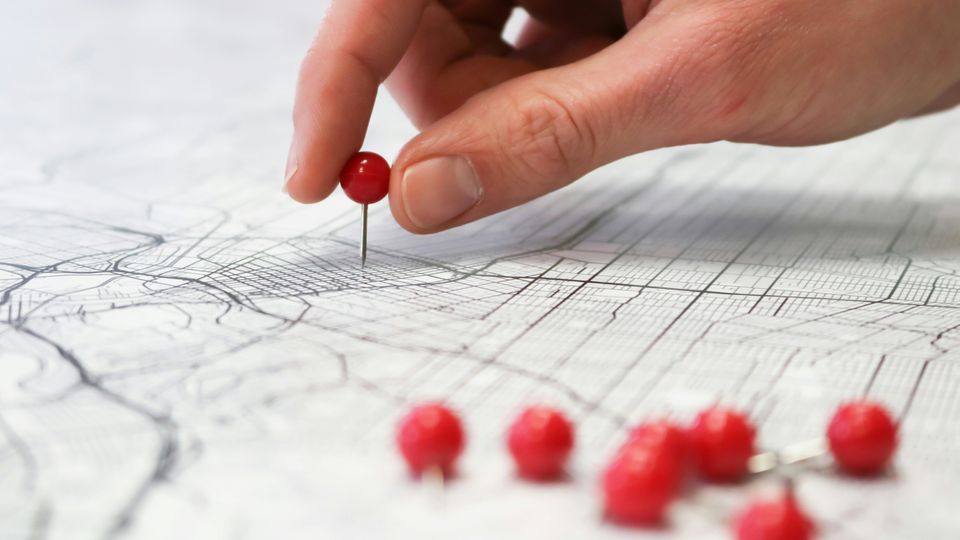 A person placing red pins in a black-and-white street map.
