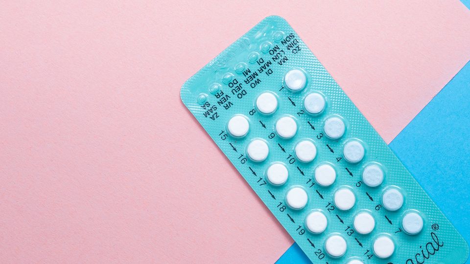 Close-up of a contraceptive pill blister pack on a pink and blue background.
