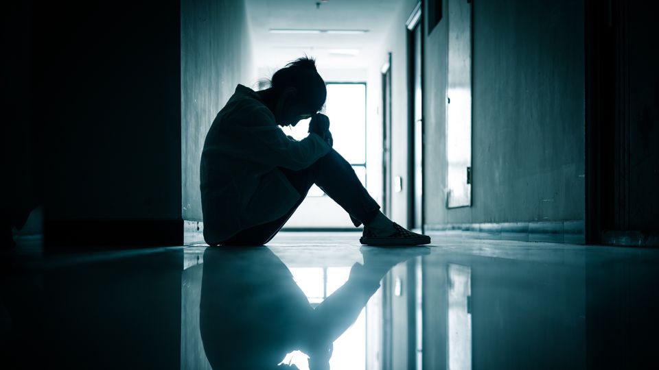 Person sitting alone in a dimly lit hallway, holding their head in their hands, reflecting feelings of depression.