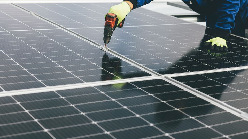 An engineer with a power drill installs a series of flat solar panels.