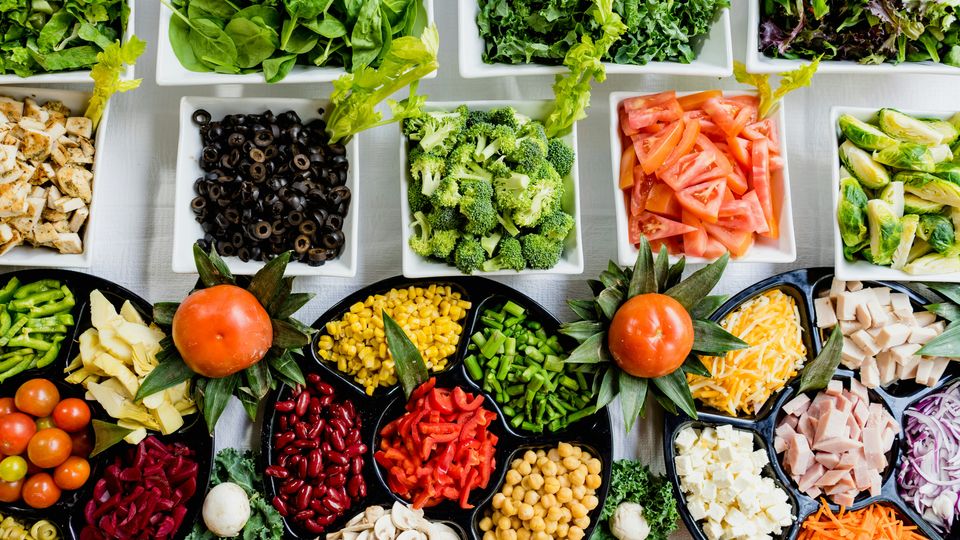 An overhead view of a salad bar, fully stocked with a colourful selection of pre-sliced fruits and vegetables.