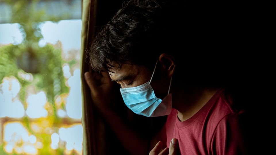 A man in a red t-shirt wearing a surgical mask.