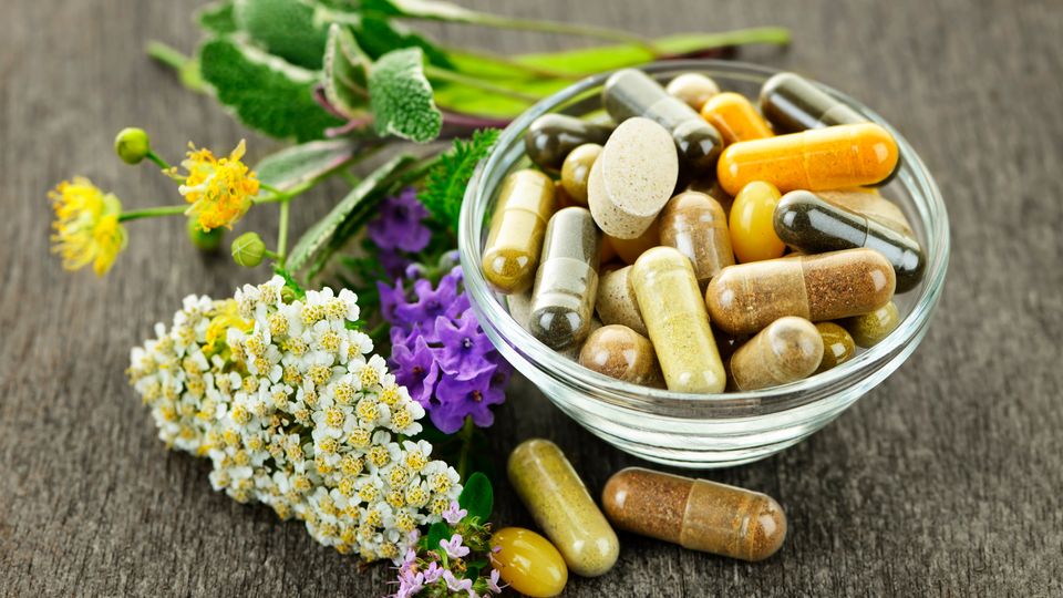 A bowel of pills next to a selection of herbs, representing natural remedies for disease.