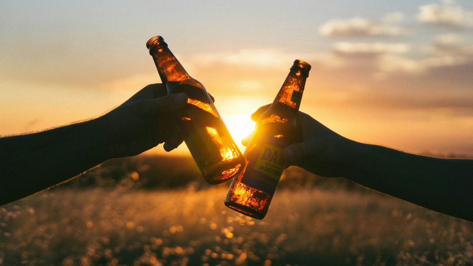 Two people toasting a pair of beer bottles at sunset.
