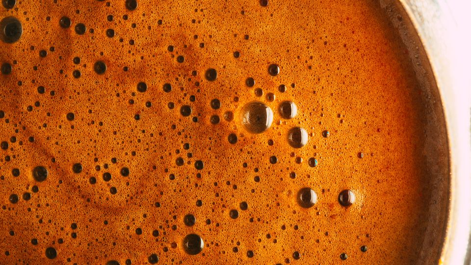 Black coffee up close, its surface brown with bubbles.