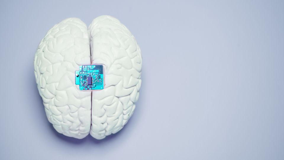 Graphic of a white brain with a blue microchip in the centre. Grey background.