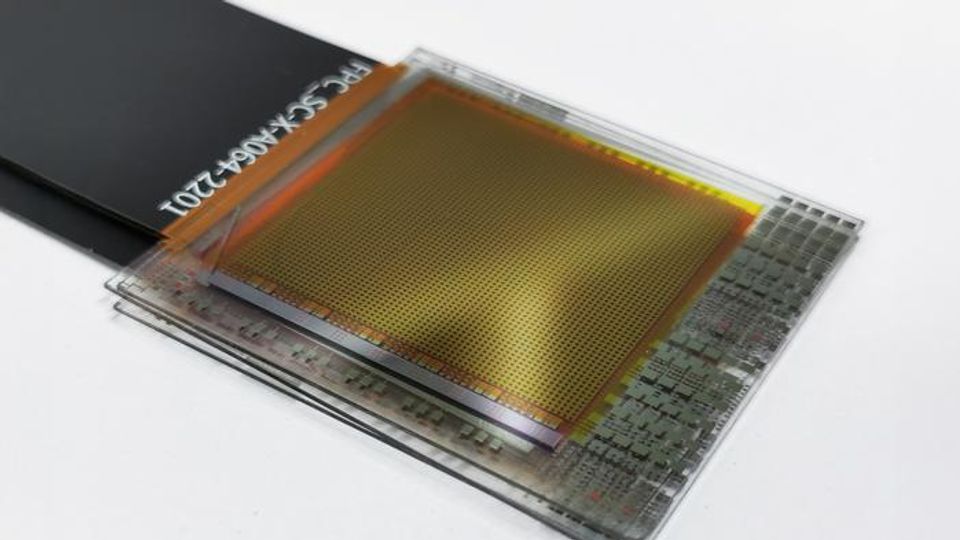 A perovskite sensor prototype. It has a wide, flat black wire coming from its left side, and its surface is full of small brown pixel-like dots.