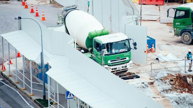 A green cement mixer truck on a concrete-floored construction site.