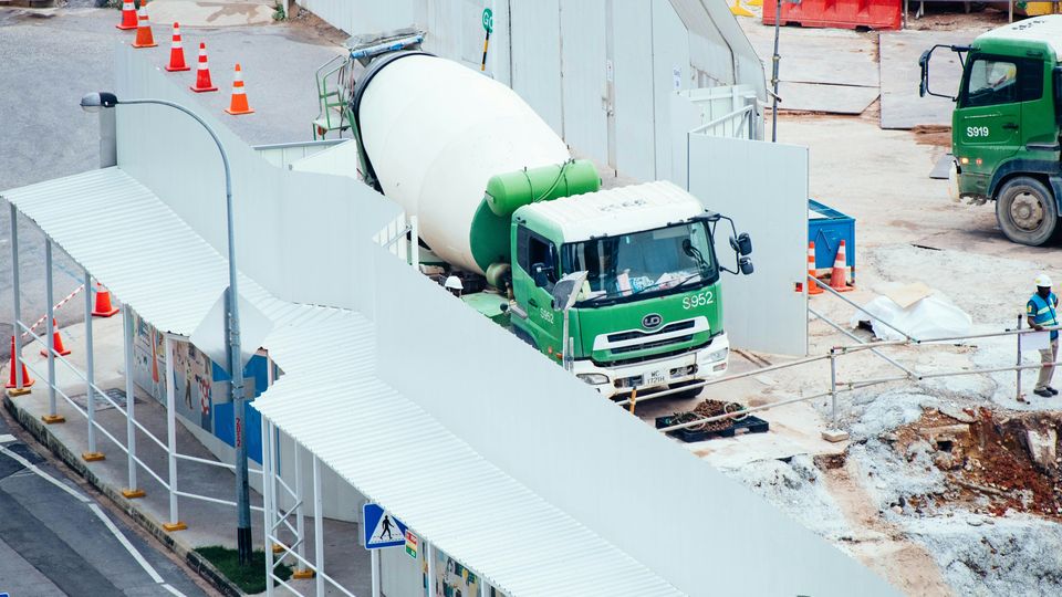 A green cement mixer truck on a concrete-floored construction site.