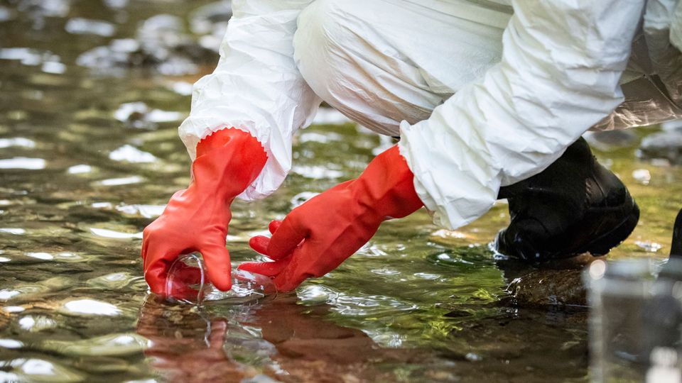 Individual in protective equipment collecting a water sample.