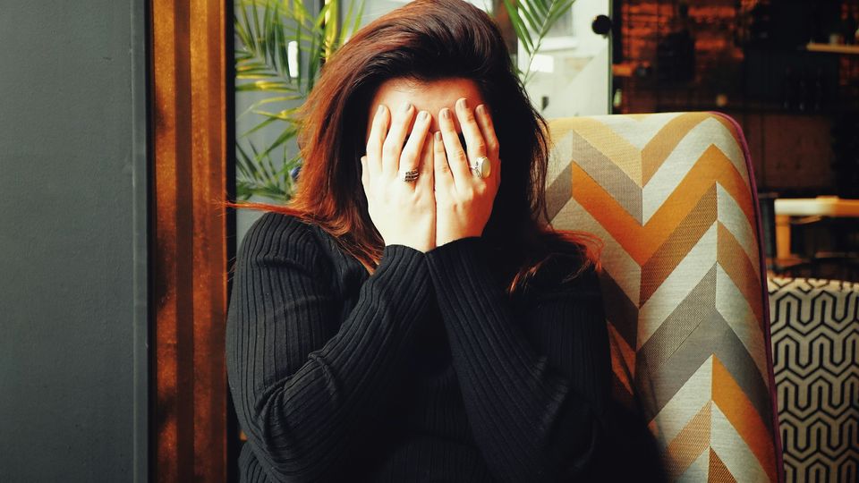A woman wearing a black sweater covers her face with her hands.