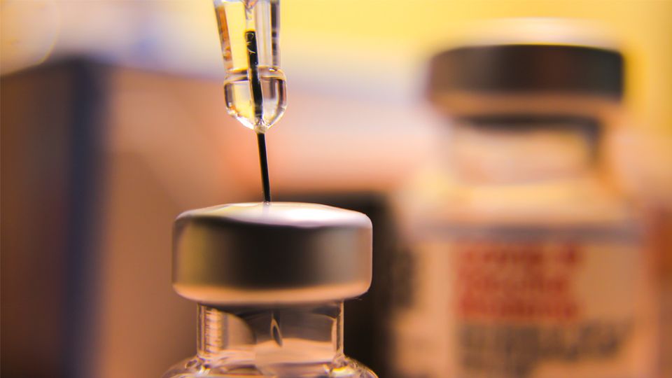 A close up of a syringe drawing liquid from a vaccine vial.