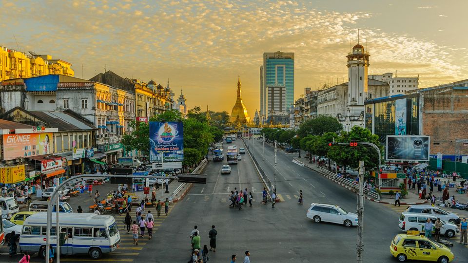 A scene from a street in Myanmar. Cars, pedestrians, buildings visible.