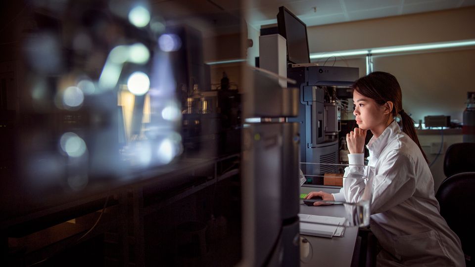 Female scientist analyzing data on a computer in a dimly lit laboratory.