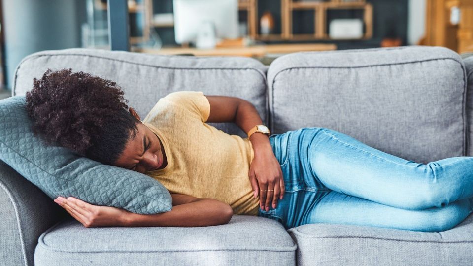 Woman lying on a couch clutching her abdomen, appearing to be in pain from endometriosis.