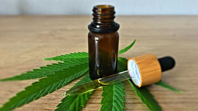 A bottle of CBD and a pipette on top of a cannabis leave on a wooden desk. 