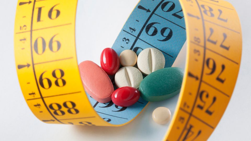 A variety of drug pills on a yellow measuring tape for weight loss.