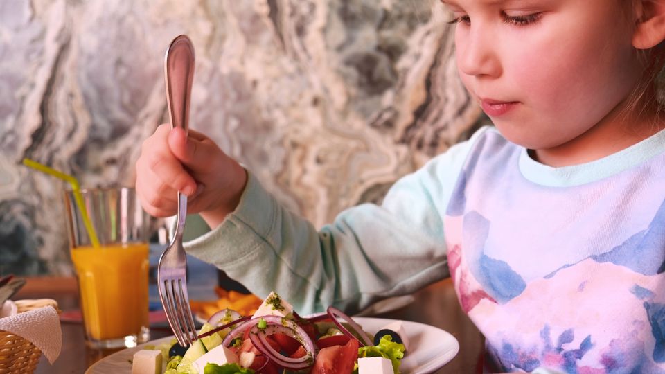 A child holds a fork over a plate of salad. Orange juice visible.