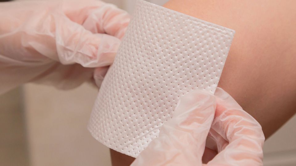 A doctor applying a bandage to a patient's wound on their kneecap.