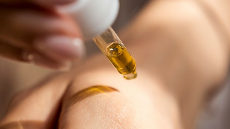 Person applying a drop of vitamin C serum from a dropper onto their skin.