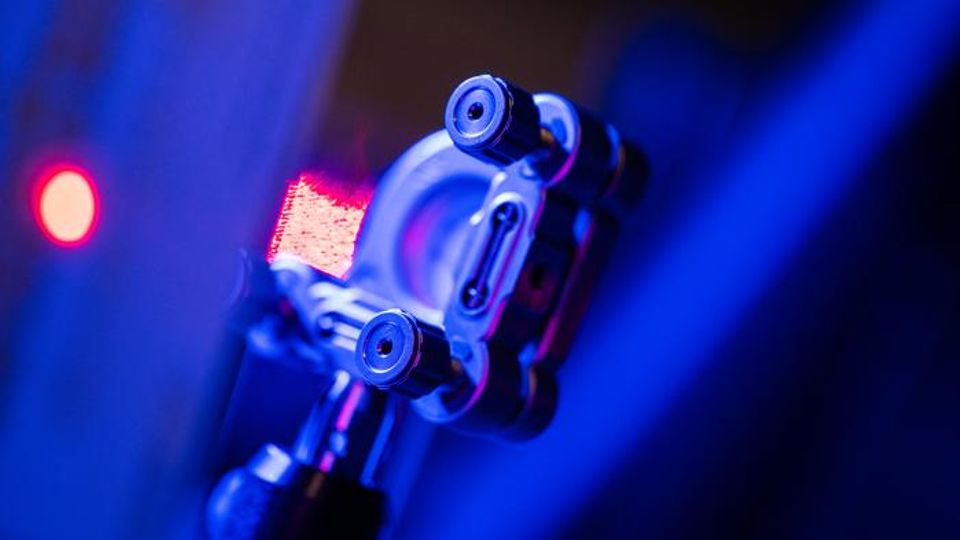 A close-up photograph of a piece of metallic lab equipment, lit up in deep blue light.