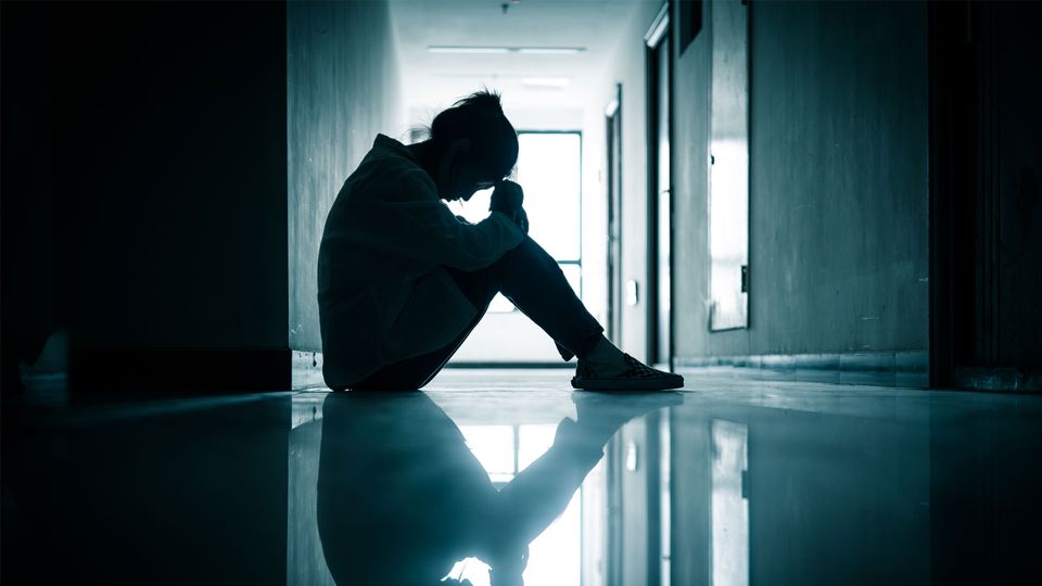 Woman sat in a dark corridor with head in hands.