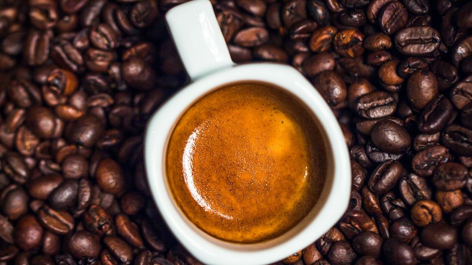 A cup of coffee rests on coffee beans, symbolizing caffeine.