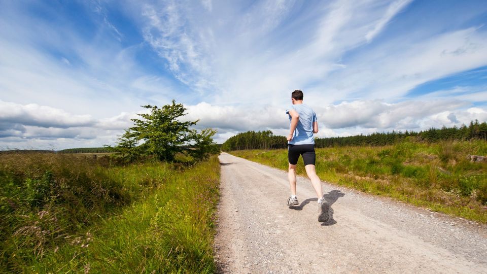 A person in shorts, t-shirt and trainers runs along a path surrounded by shrubbery.